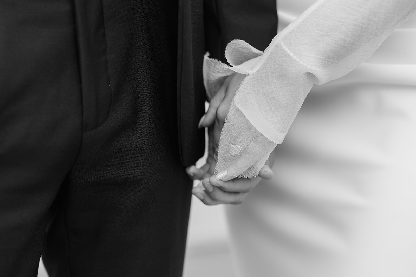 Black and white close-up of the couple holding hands, highlighting the bride's delicate sheer sleeve.